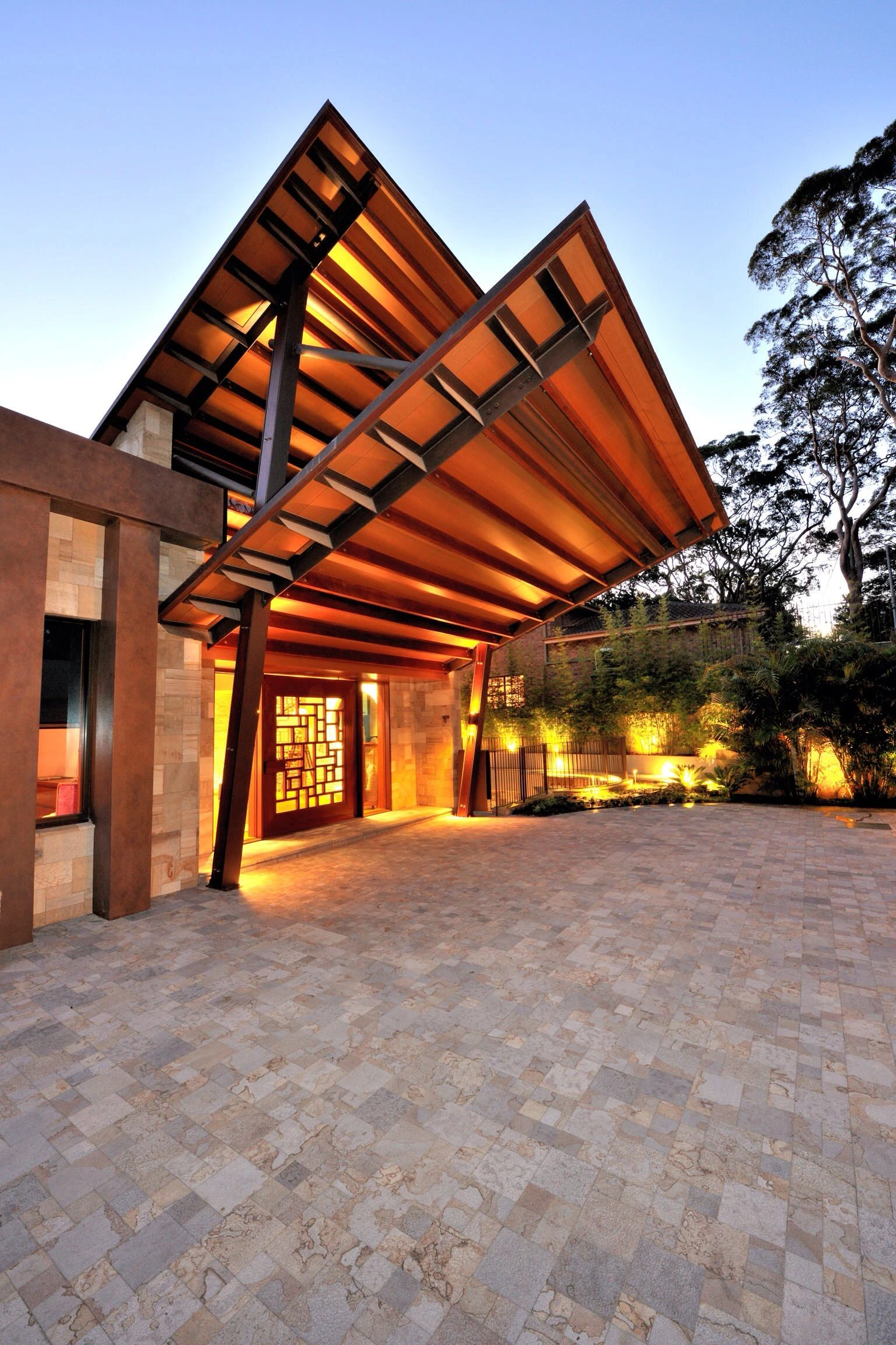 Upscale concrete driveway in Southlake TX with decorative stone pavers, illuminated by ambient lighting under a dramatic architectural canopy, creating an elegant entrance with warm evening ambiance.