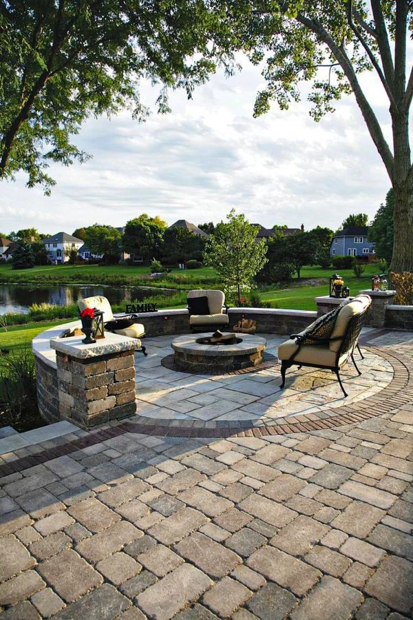 Elegant concrete patio in Southlake TX overlooking a pond, showcasing multi-level design with stone pillars, curved retaining walls, fire pit area, and premium paver installation creating a sophisticated outdoor living space.