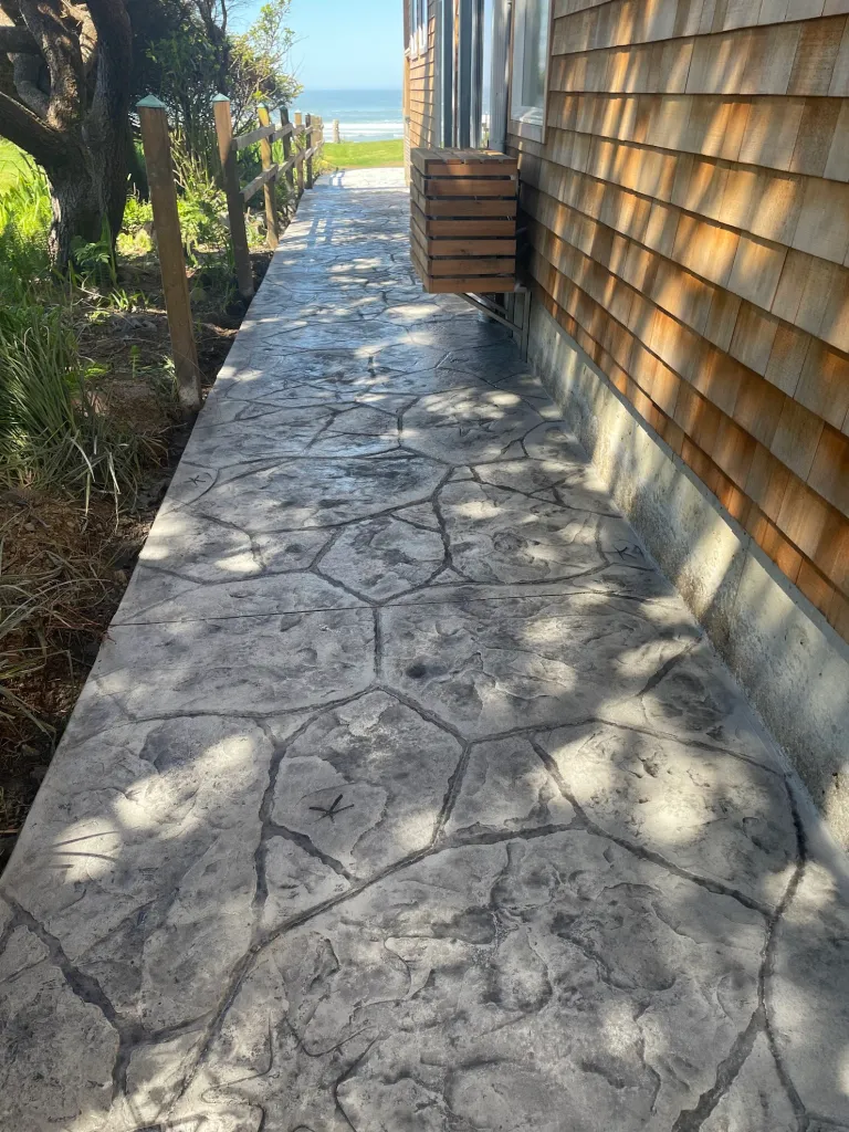 Stamped concrete in Southlake TX showcasing a slate-textured walkway with natural stone pattern, leading to oceanfront view, complemented by cedar shake siding and coastal landscaping.